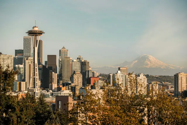 Downtown towers in warm evening light seen from Kerry Park, with snow-capped Mount Rainier in the haze to the right and autumn trees in front.